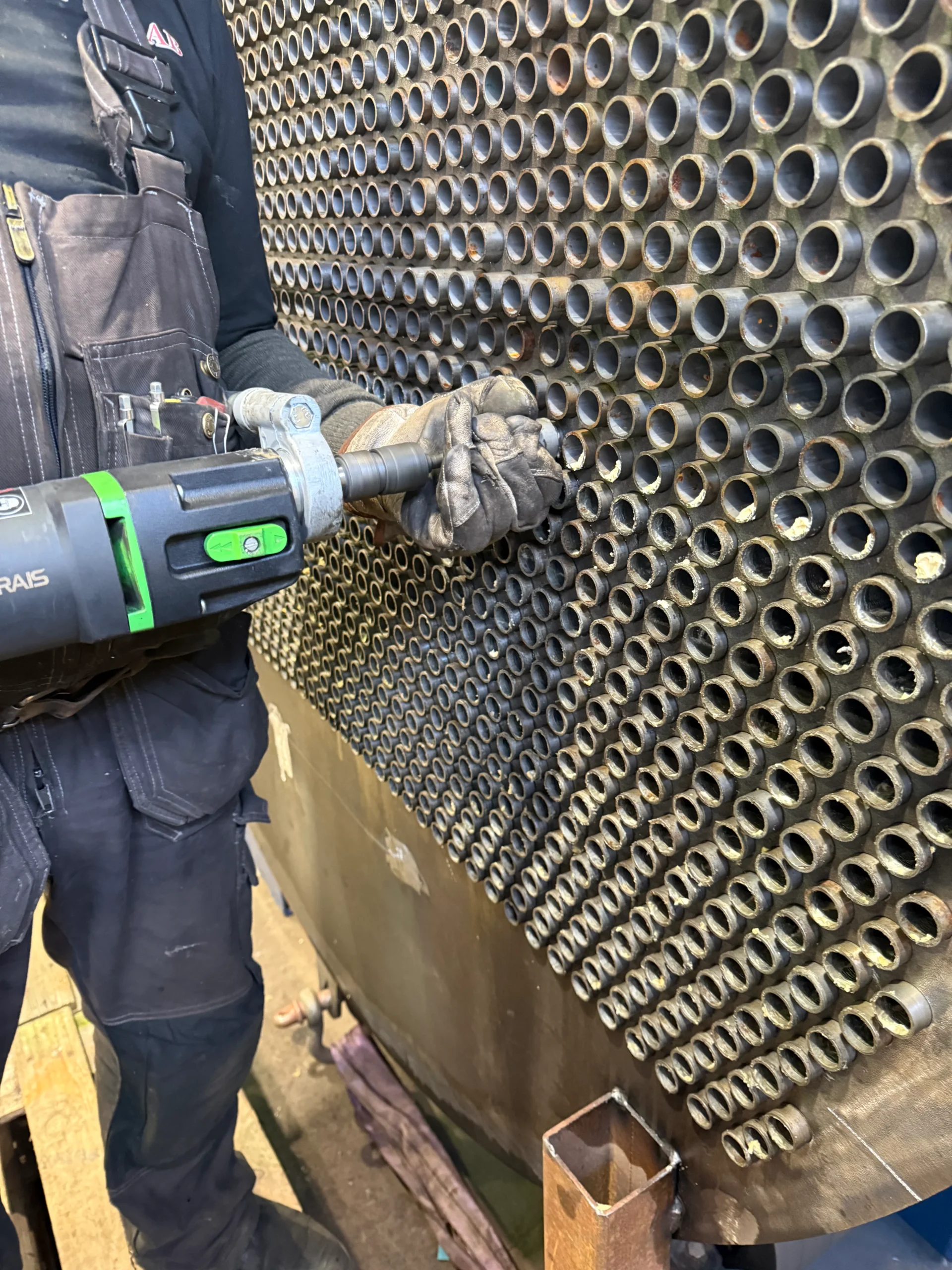 Operatör utför tubinvalsning i tubplåt på värmeväxlare med valsverktyg i industriell miljö.