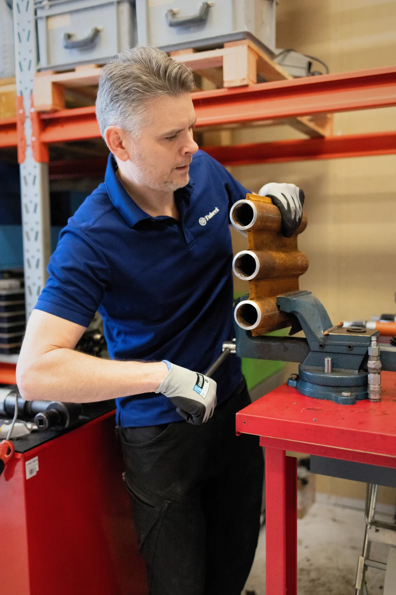 Tekniker på Tubeck AB som arbetar med ett rörverktyg och kontrollerar en rörkomponent i en verkstadsmiljö för rörbearbetning.